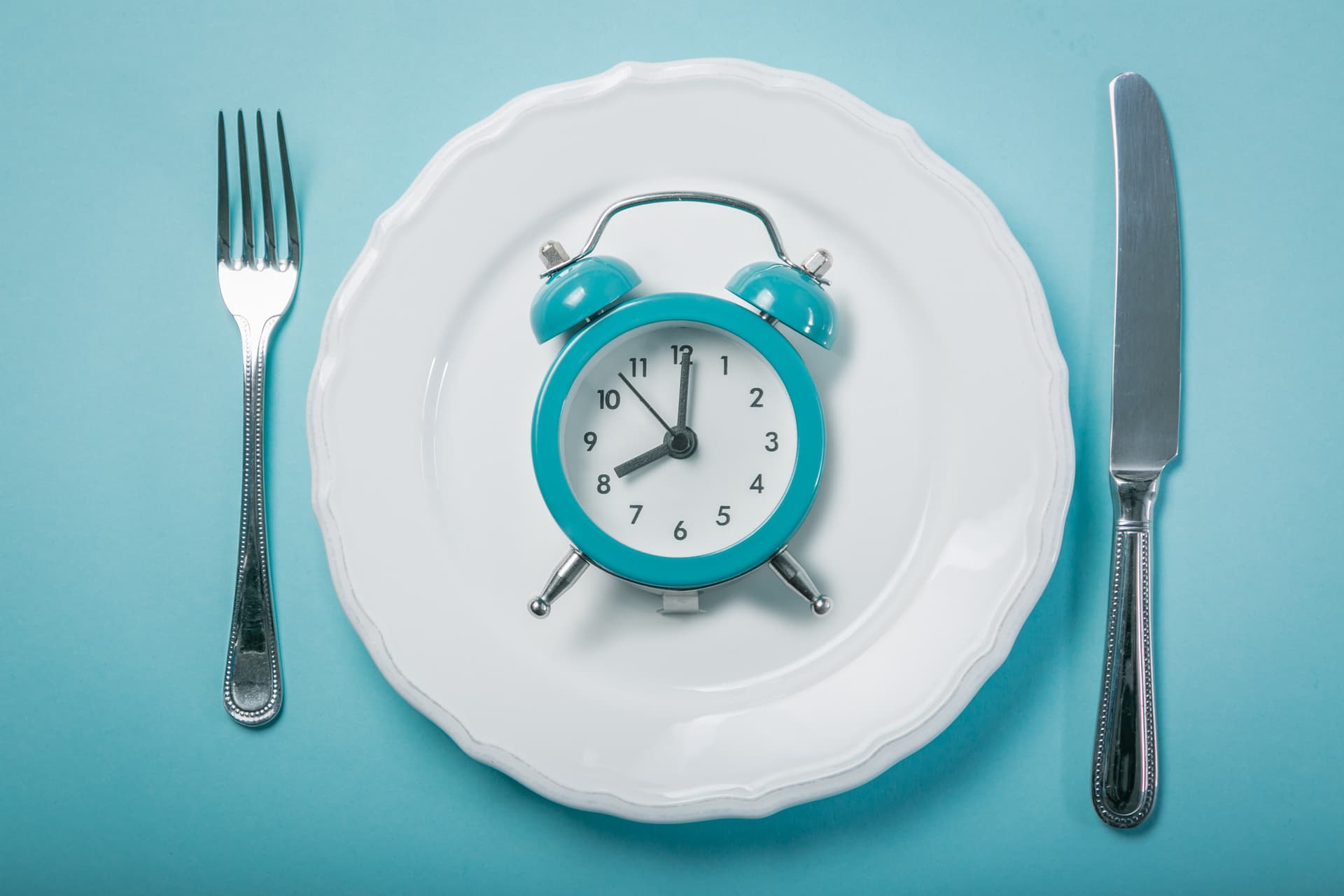 Alarm clock on an empty plate between a fork and knife