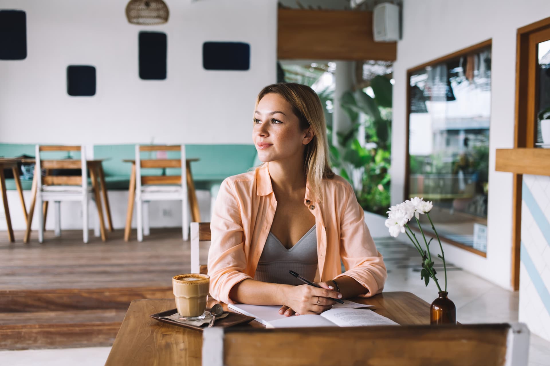 Woman journaling at a cafe table while reflecting on her food patterns.