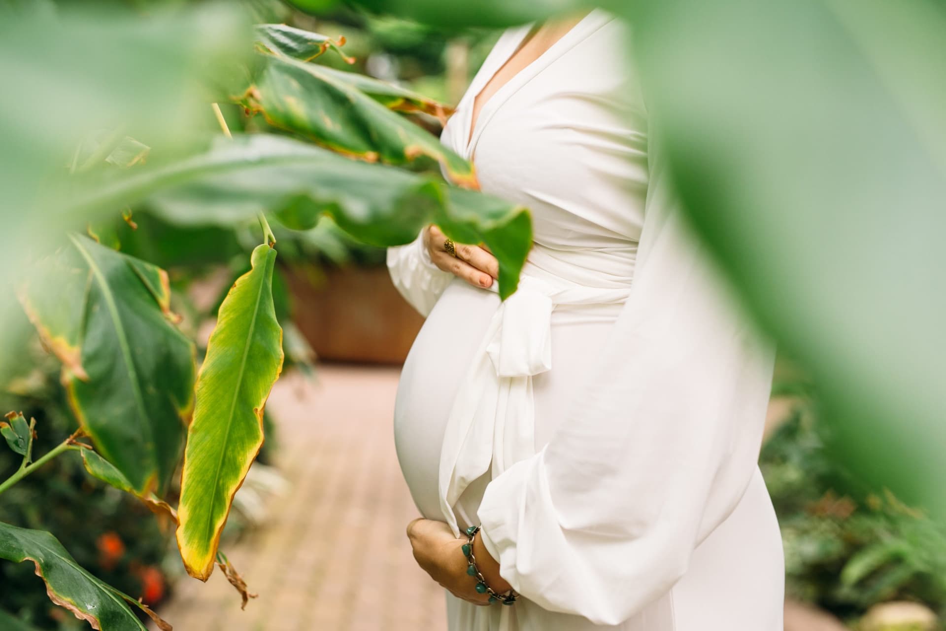 Expectant mother holding her belly among greenhouse plants.