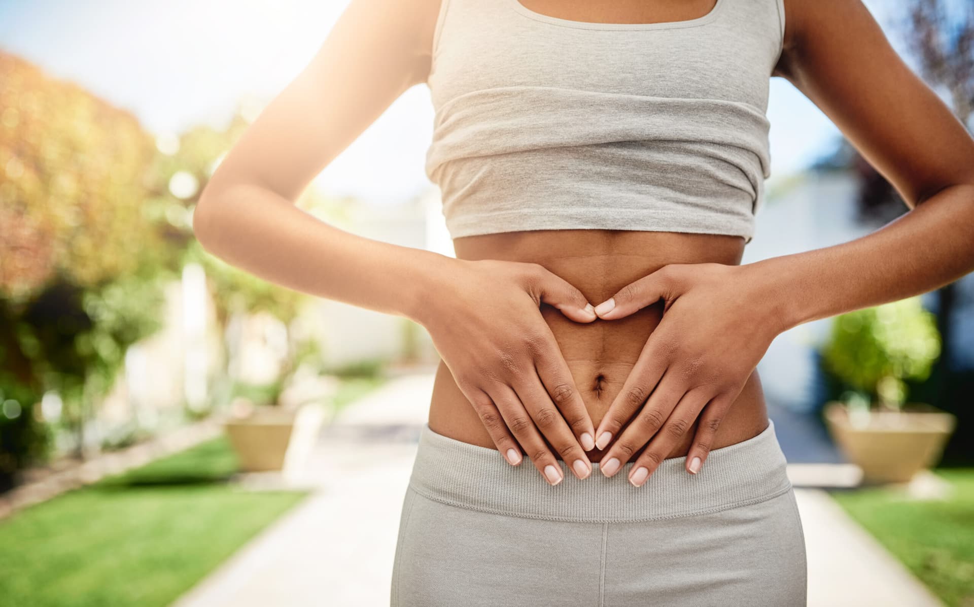 Woman framing her stomach with her hands in a heart shape outdoors.