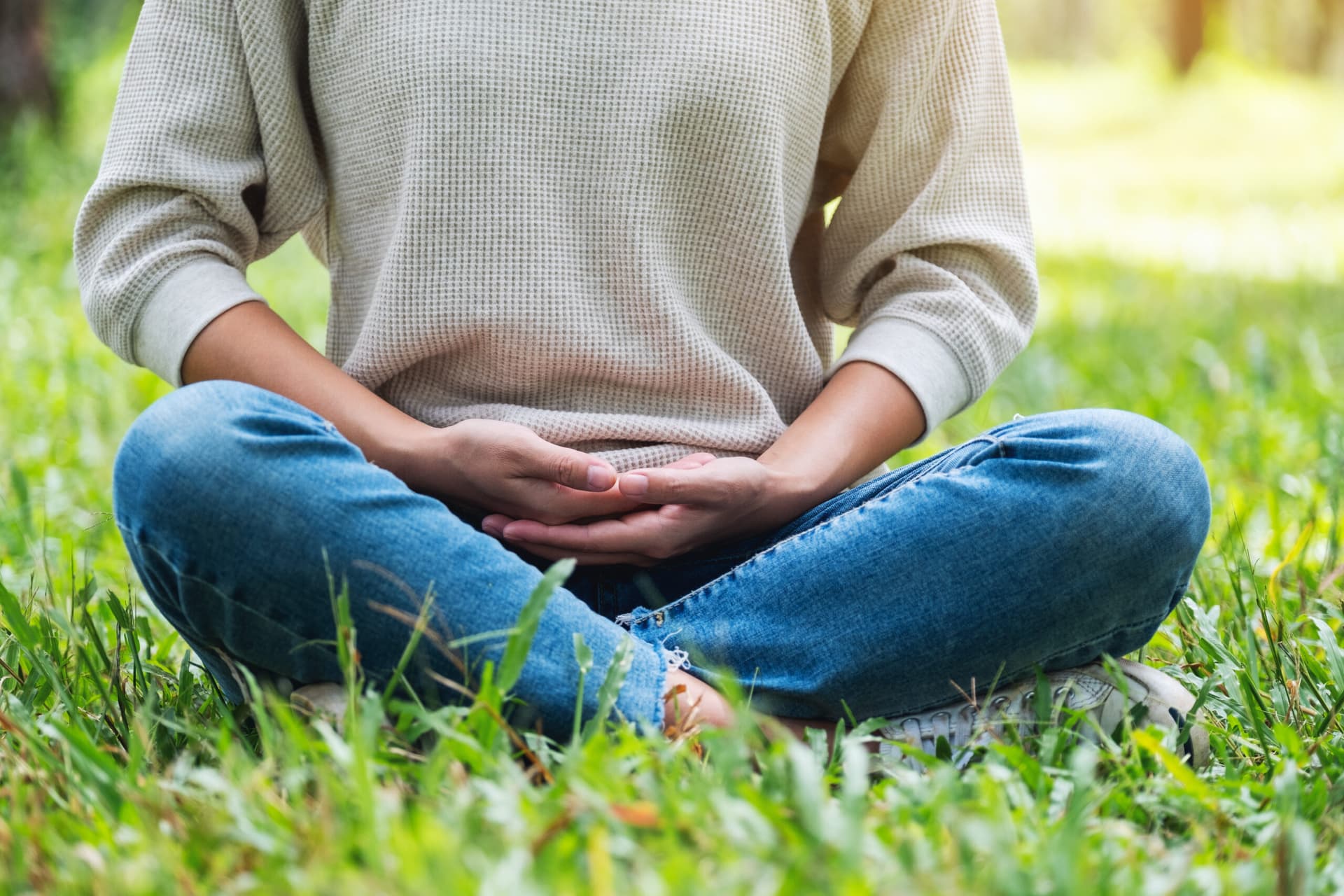 Woman sitting cross-legged on the grass with her hands resting over her stomach.