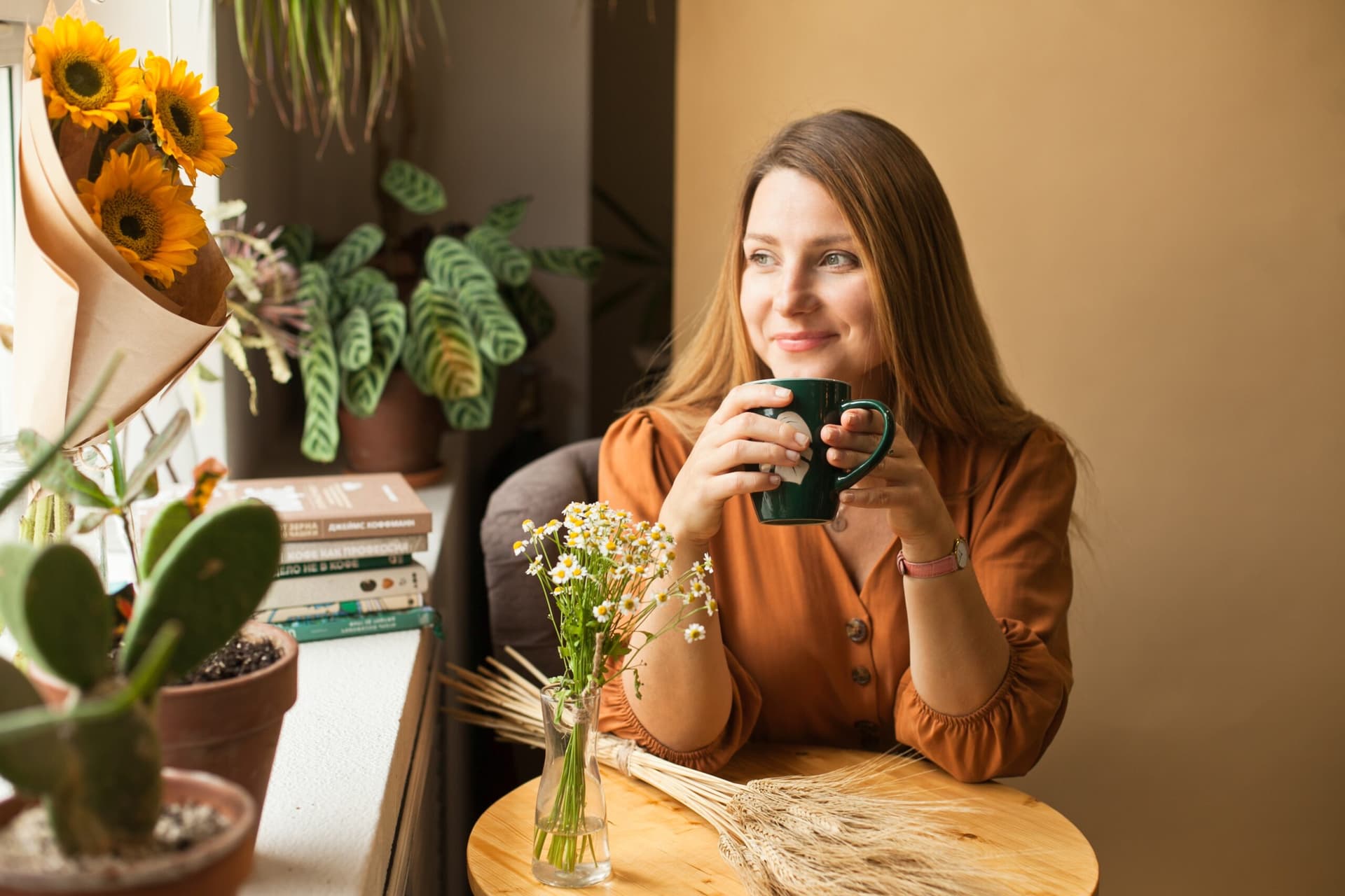 Woman smiling at a table in a flower-filled cafe.