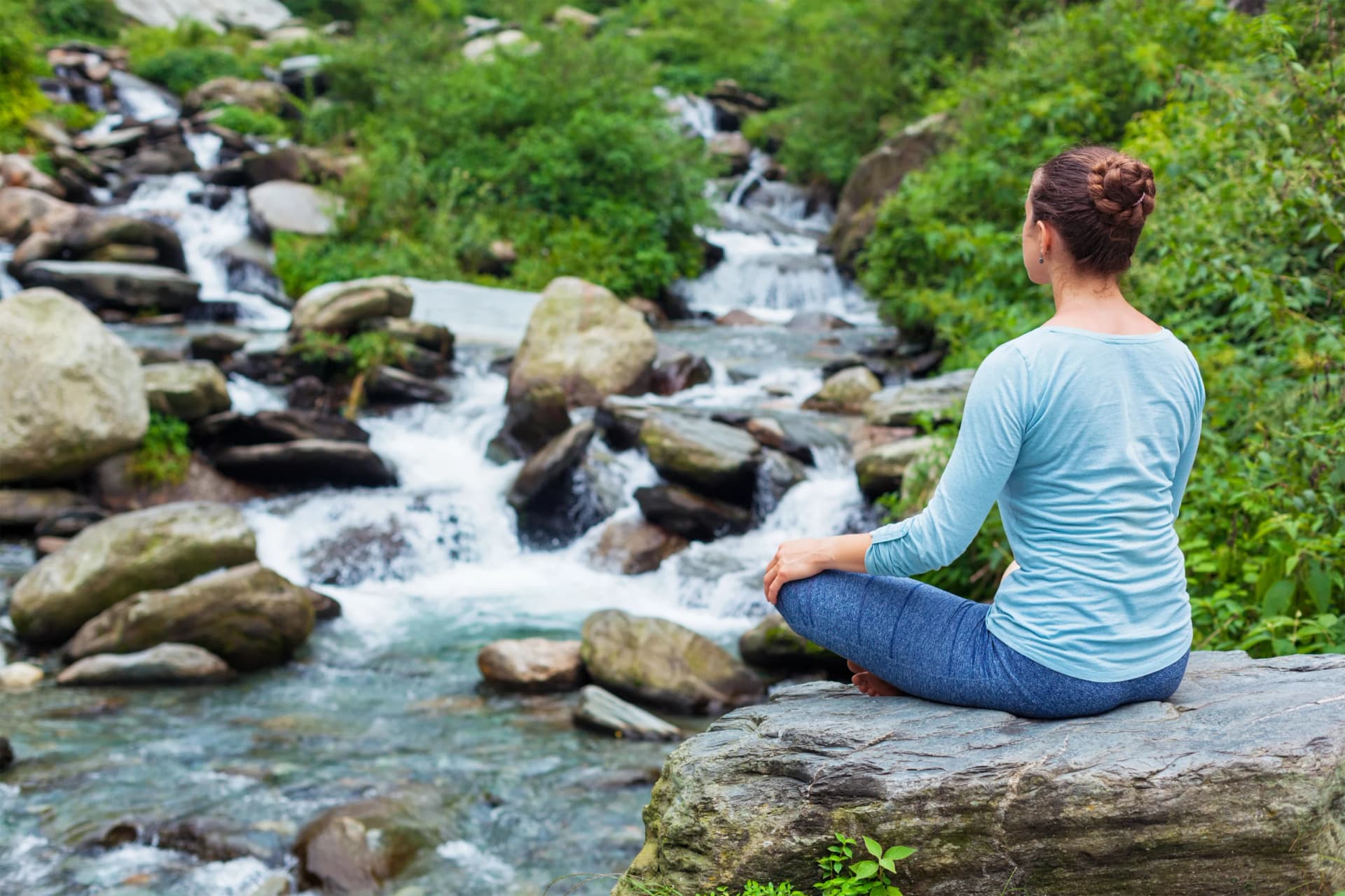 Woman sitting in padmasana yoga pose outdoors.