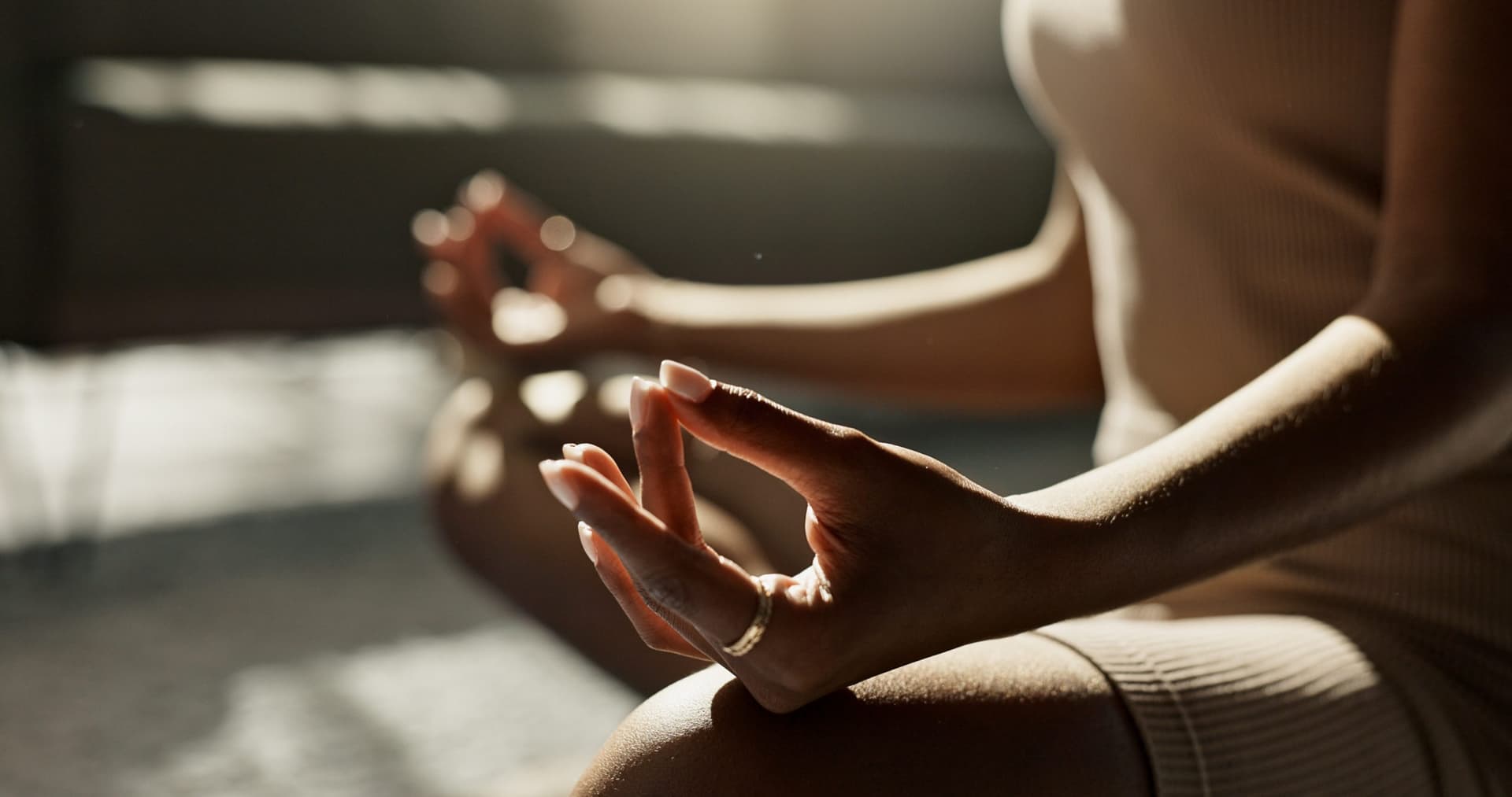 Close-up of a woman's hands resting in a meditation mudra as she sits cross-legged on the floor